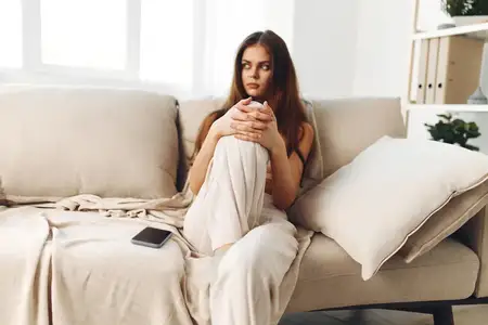 Счастливая женщина держит смартфон, улыбается и наслаждается досугом в уютной гостиной дома