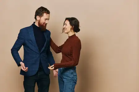 Мужчина и женщина, пара в отношениях, улыбаются и взаимодействуют на бежевом фоне, демонстрируя настоящие отношения между людьми
