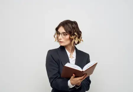 Женщина в классическом костюме с открытой книгой и очками на лице, кадрированный вид