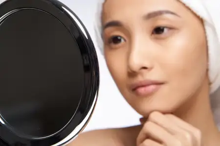 Женщина держит в руках зеркало и любуется своей чистой кожей
