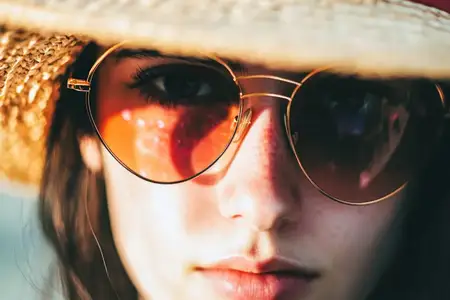 Этот крупный план портрета молодой женщины с безмятежным выражением лица, в соломенной шляпе и стильных солнцезащитных очках, идеально подходит для летних изображений и изображений образа жизни