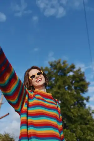 Улыбающаяся женщина в радужном свитере и солнцезащитных очках на открытом воздухе, портретный повседневный наряд