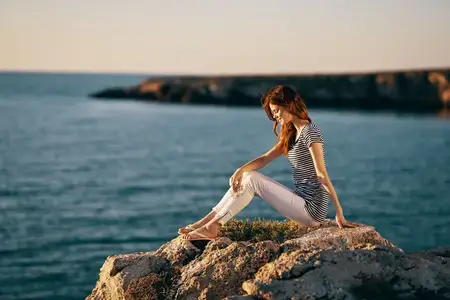 Женщина у моря в горах на большом камне, морской пейзаж на закате