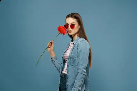 Женщина в солнцезащитных очках позирует крупным планом, держа красный цветок у лица