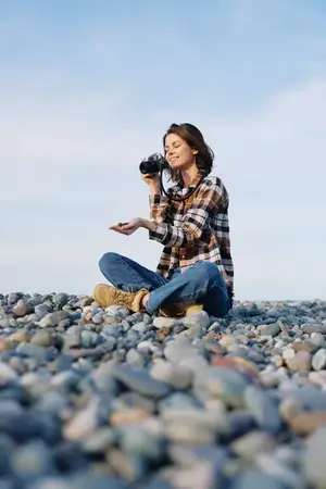 Уличный фотограф на камнях у берега фокусируется через камеру