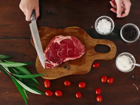 Женщина с ножом в руке нарезает свежий стейк для жарки на кухне