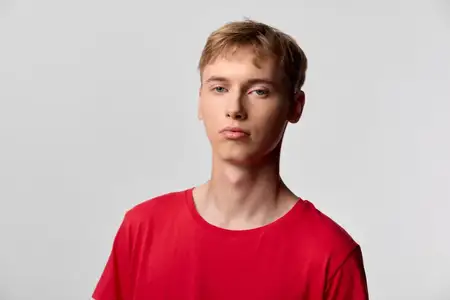 Студийный снимок молодого человека в красной футболке со спокойным взглядом и однотонным фоном