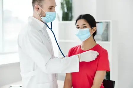 Пациентка проходит осмотр у врача в медицинской маске, защитных перчатках и со стетоскопом