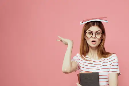 Красивая студентка держит книги, жестикулирует руками на розовом фоне