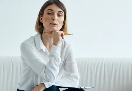 Женщина сидит на диване в светлой комнате, на ней рубашка и бумаги
