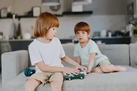 Мальчик и девочка играют в воображаемые игры с игрушечными машинками на удобном диване, что подчеркивает тему детского удивления и невинности в современном домашнем интерьере