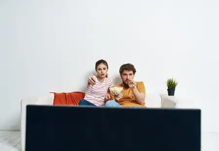 Весёлая молодая пара смотрит фильм, занимаясь семейным отдыхом с попкорном