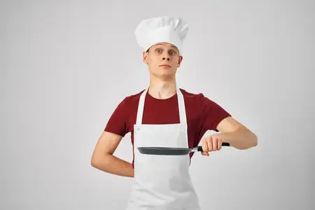 Мужчина-повар держит сковороду в руках, профессиональное приготовление пищи на кухне