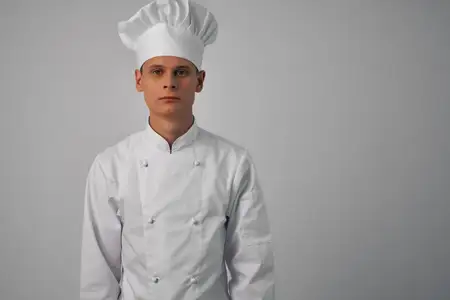 Весёлый шеф-повар мужского пола работает на кухне ресторана, занимаясь приготовлением блюд