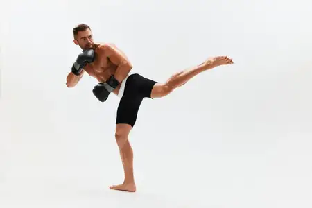 Спортивный мужчина, культурист, позирует в боксёрских перчатках с обнажённым торсом и рельефным прессом в полный рост на фоне