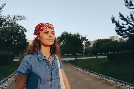 Женщина в стиле современной богемно-вестерн джинсовой уличной моды с красной банданой уверенно стоит на дорожке среди деревьев на открытом воздухе