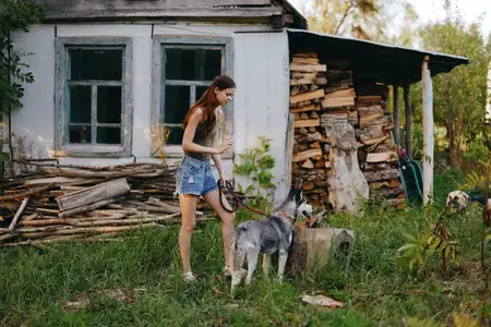 Женщина и её хаски весело играют на свежем воздухе в парке среди деревьев, улыбаются, показывая зубы, во время осенней прогулки со своим питомцем