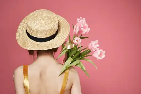 Женщина в шляпе с букетом цветов, вид сзади, декор, розовый фон