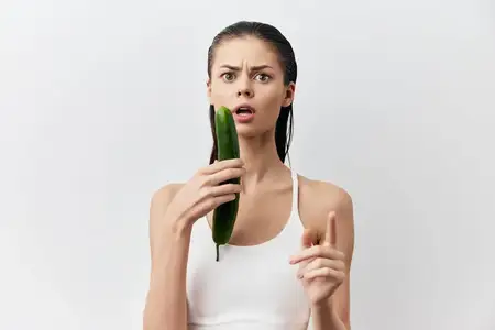 Удивленная женщина держит огурец, выражая шокированное выражение лица