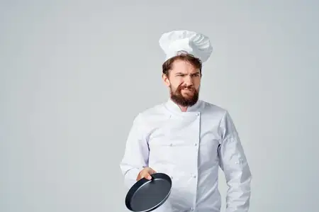 Мужчина в форме шеф-повара с кухонными принадлежностями на светлом фоне
