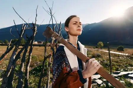 Женщина в сельской местности, поле, топор и забор с горами и ярким солнечным светом