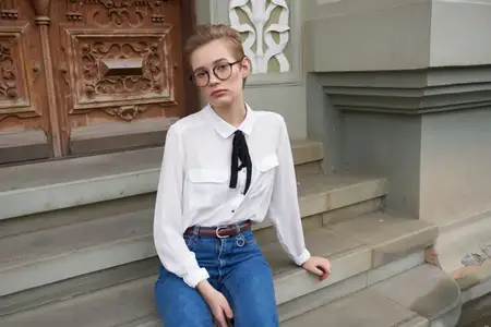 Привлекательная женщина в джинсах, кроссовках и рубашке сидит на ступенях возле здания института