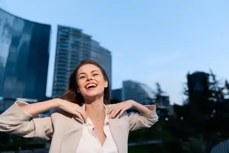 Радостная деловая женщина излучает уверенность в стильном наряде на фоне современной архитектуры, что подчеркивает яркий и динамичный образ жизни