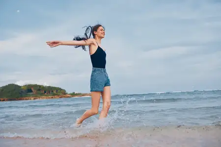 Женщина бежит по пляжу на закате, её длинные волосы развеваются