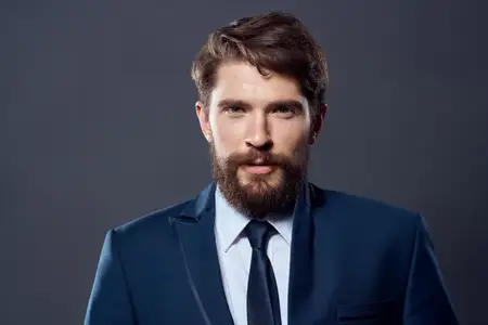 Бородатый мужчина в пиджаке и галстуке на тёмном фоне