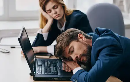 Коллеги по работе спят за столом перед ноутбуком, усталость и отдых