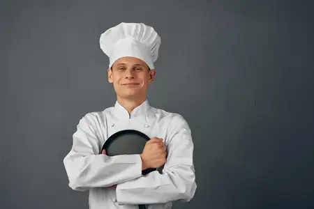 Шеф-повар обнимает сковороду на кухне на тёмном фоне