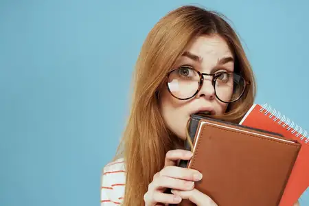 Энергичная студентка с блокнотами и в очках позирует на синем фоне