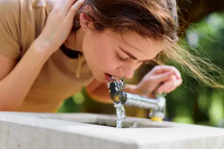 Женщина пьёт воду из уличного фонтана, крупный план портрета, показывающий гидратацию и освежение
