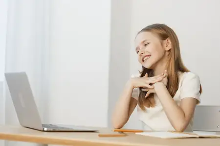 Счастливая маленькая девочка работает с ноутбуком в аккуратном домашнем офисе