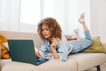 Улыбающаяся женщина работает фрилансером за ноутбуком в уютном домашнем кабинете