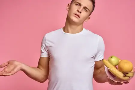 Мужчина с фруктами в руках на розовом фоне, здоровая пища, витамины, розовый фон, белая футболка, модель