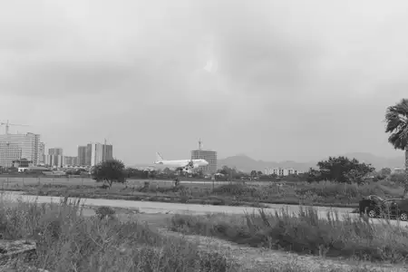 Пейзаж на окраине города: широкое поле, далекие здания, бледные облака и пасущаяся лошадь, создающие тихую мрачную композицию, сочетающую сельское спокойствие с городской активностью