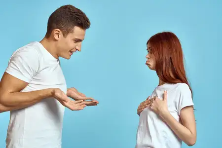 Молодая женщина и мужчина, между которыми возникли разногласия, на голубом фоне; кадр обрезан, показана влюблённая пара