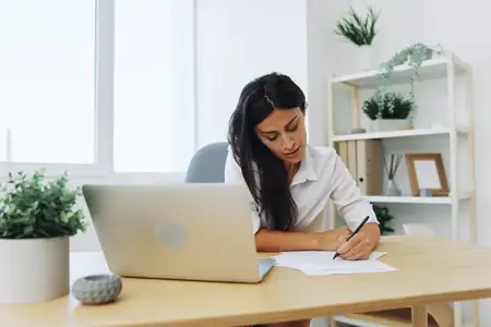 Женщина работает и учится, записывая текст на бумаге ручкой и проверяя ошибки