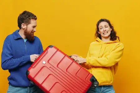 Женщина и мужчина улыбаются, в руках чемоданы — жёлтый и красный, улыбаются весело и криво, жёлтый фон, отправляются в путешествие, семейный отпуск, поездка, молодожёны