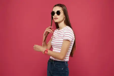 Симпатичная женщина в полосатой футболке и солнцезащитных очках на розовом фоне, гламур
