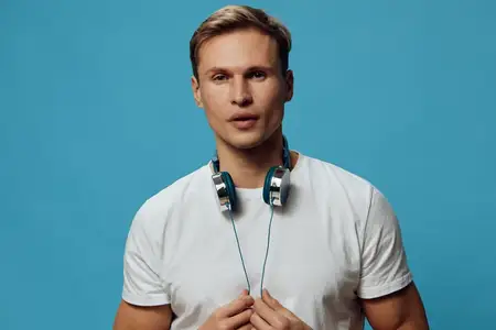 Портрет молодого человека с наушниками на шее, одетого в белую повседневную футболку, смотрящего прямо в камеру с нейтральным выражением лица