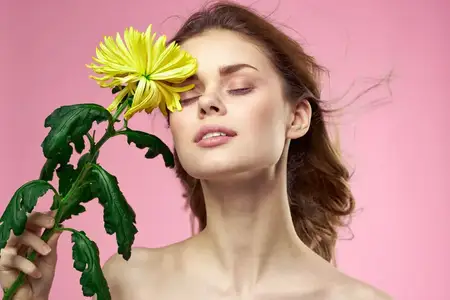 Красивая девушка с жёлтым цветком на розовом фоне, обнажённые плечи, макияж