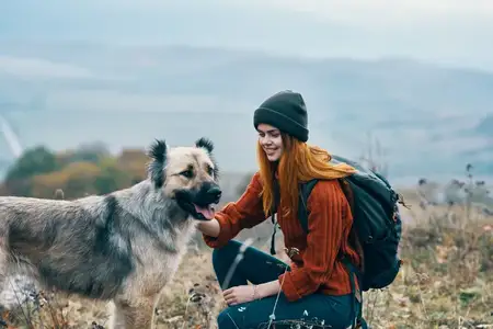 Жизнерадостная женщина-туристка выгуливает собаку на природе в горном пейзаже