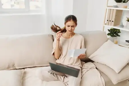 Улыбающаяся женщина работает за ноутбуком в уютной гостиной, наслаждаясь фриланс-работой и современными технологиями