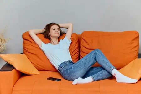 Женщина болтает по смартфону, сидя на оранжевом диване