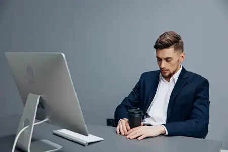 Уставший красивый бизнесмен с чашкой кофе работает за компьютером в офисе