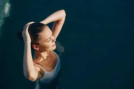 Спокойная женщина наслаждается тихим моментом у бассейна, вода окружает ее, а залитые солнцем блики мерцают