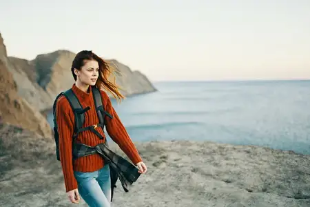 Девушка с рюкзаком на фоне гор и моря