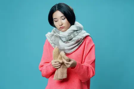 Азиатская женщина в теплом свитере, шарфе и варежках на синем фоне, обрезанный вид
